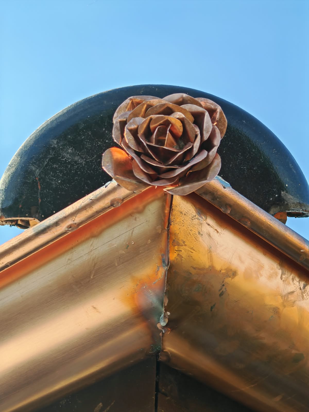 Rose façonnée à la main en cuivre au sommet d’un ornement de toiture, création artisanale SkySafe Toitures