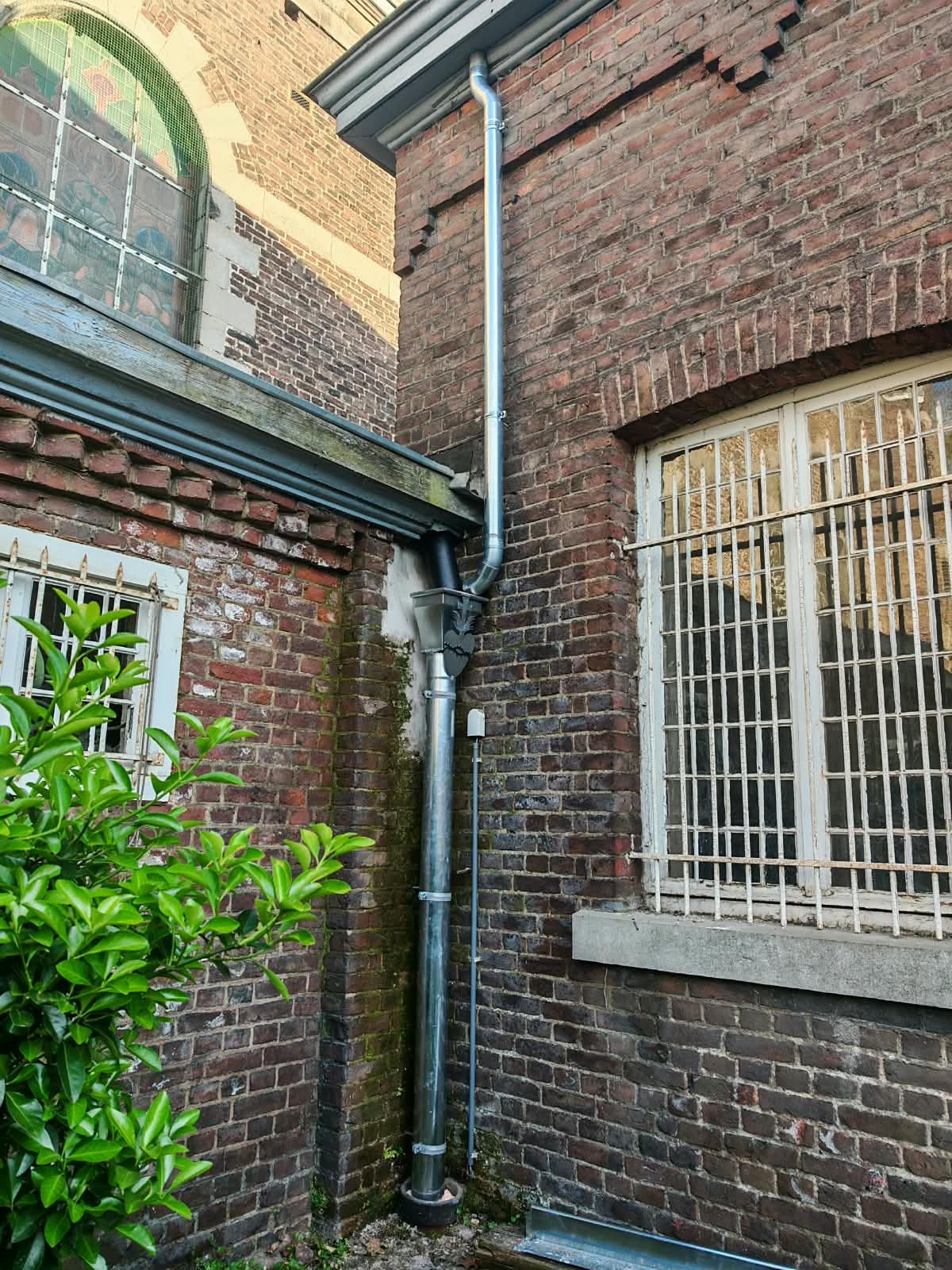 Descente d'eaux pluviales posée le long d'une façade en brique par SkySafe Toitures
